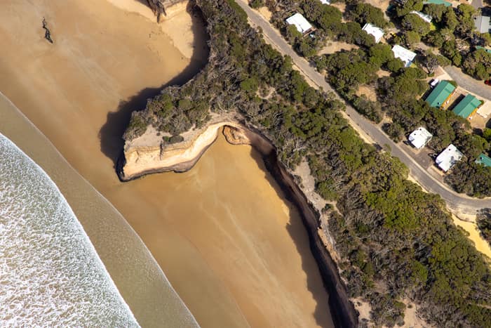 Aerial view of a sandy beach, eroded coastal cliffs, bushland and nearby houses along the Anglesea coastline in Victoria.