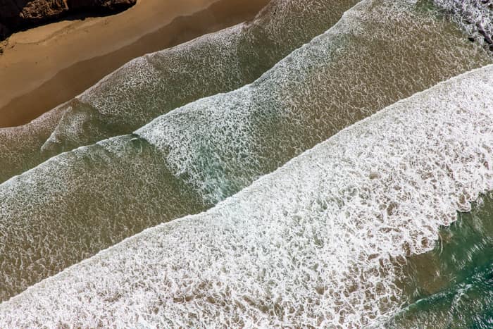 Aerial view of white surf breaking over shallow water beside a sandy beach on the Anglesea coastline in Victoria.