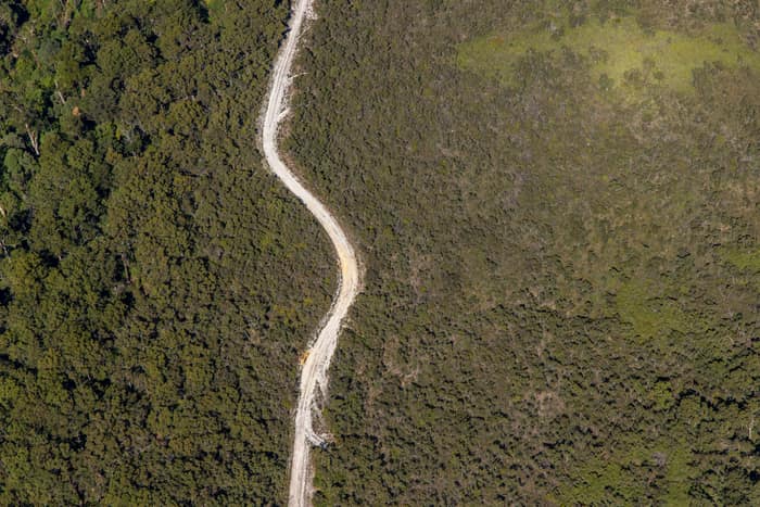 Aerial view of a winding unsealed bush track cutting through dense native vegetation near Carlisle River in the Otway Ranges, Victoria.