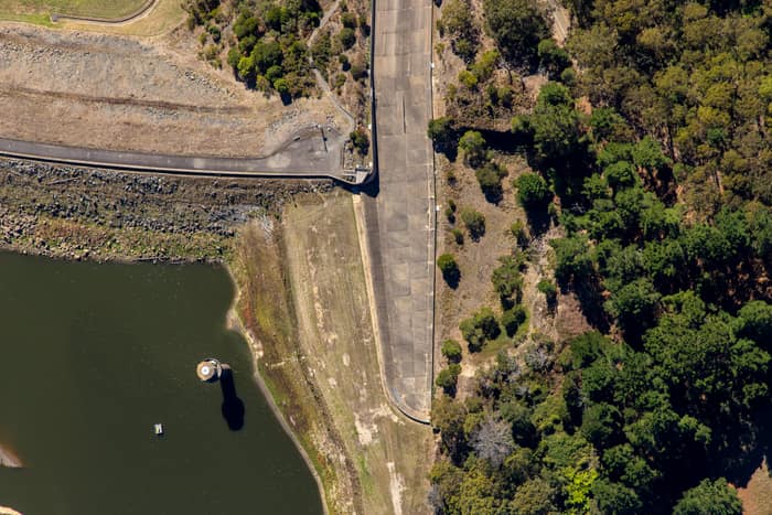 Aerial view of the West Barwon Reservoir dam wall at Forrest, showing the reservoir edge, concrete roadway and surrounding forest.