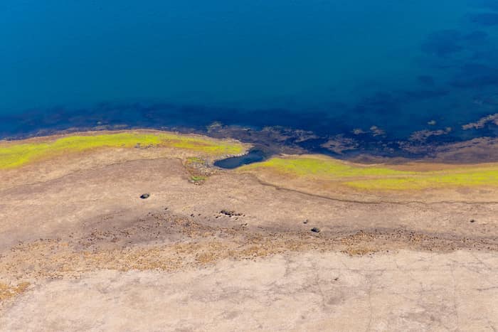 Aerial view of Lake Modewarre shoreline at Modewarre VIC, showing blue water, exposed lakebed and yellow-green vegetation along the shallow edge.