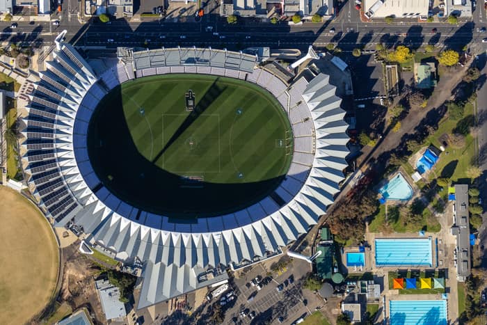 Aerial view of GMHBA Stadium at Kardinia Park in South Geelong, showing the oval playing field, grandstands, surrounding streets, car parks and nearby swimming pools.