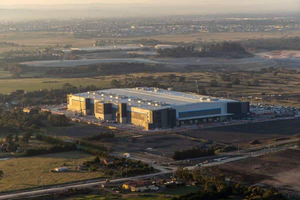Aerial view of a large industrial warehouse complex surrounded by roads, car parks, open land and developing estates in Mickleham, Victoria.