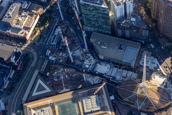 Aerial construction-progress view of the Melbourne Arts Precinct Transformation, with tower cranes, concrete works and the Arts Centre Melbourne spire in Southbank, Victoria.