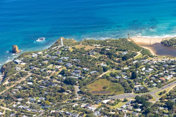 Aerial view of Split Point Lighthouse and Eagle Rock at Aireys Inlet, showing coastal homes, turquoise ocean, beaches and the nearby creek estuary.