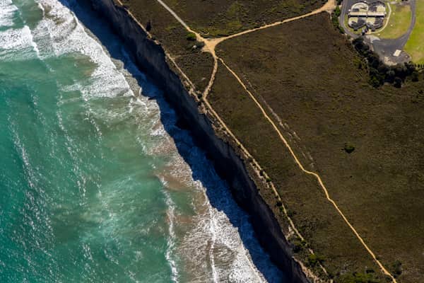 Aerial view of Anglesea coastal cliffs above Bass Strait, with surf breaking along the shore, clifftop walking tracks and scrubland on Victoria's Surf Coast.