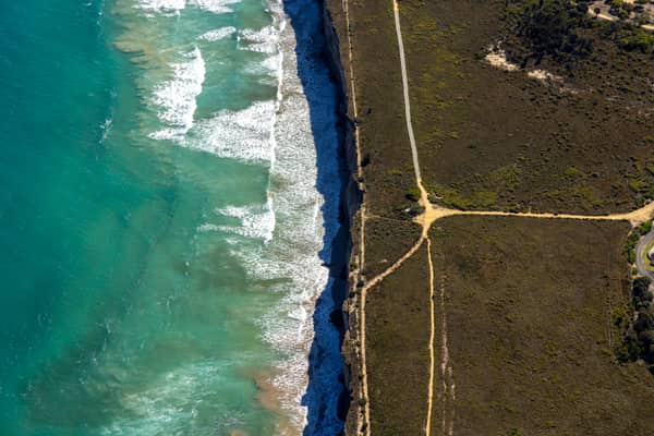 Aerial view of the Anglesea ocean cliffs beside Bass Strait, with turquoise surf, wave lines, coastal heathland and sandy walking tracks in Anglesea Victoria.