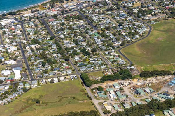 Aerial view of Apollo Bay Beach, coastal homes, residential streets, open paddocks and light industrial buildings in Apollo Bay, Victoria.