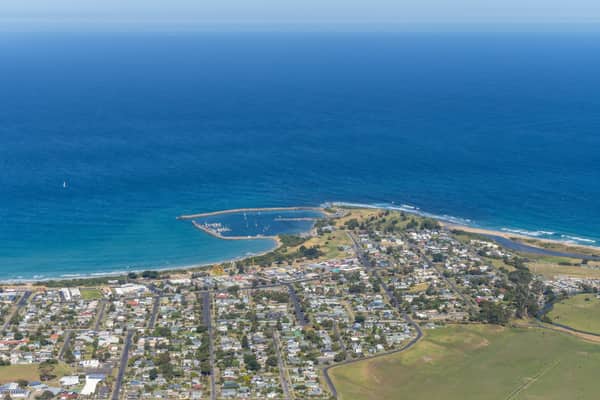 Aerial view of Apollo Bay Harbour with breakwaters, marina berths, coastal homes, beaches and the Southern Ocean at Apollo Bay VIC.