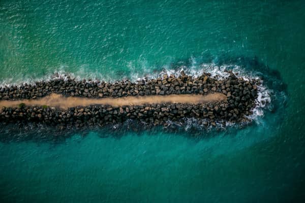 Aerial view of the Fingal Head breakwater with a rock wall and narrow walking track extending into clear turquoise ocean water at Fingal Head, New South Wales.