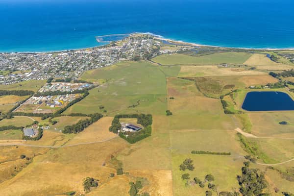 Aerial view of Apollo Bay township and coastline in Victoria, with farmland, rural properties, a farm dam, beaches and blue ocean around the harbour.