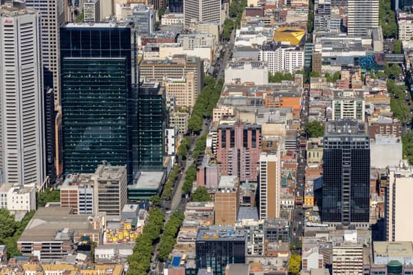 Aerial view of Bourke Street and dense Melbourne CBD city blocks with high-rise office towers, streets, rooftops and tree-lined roads.