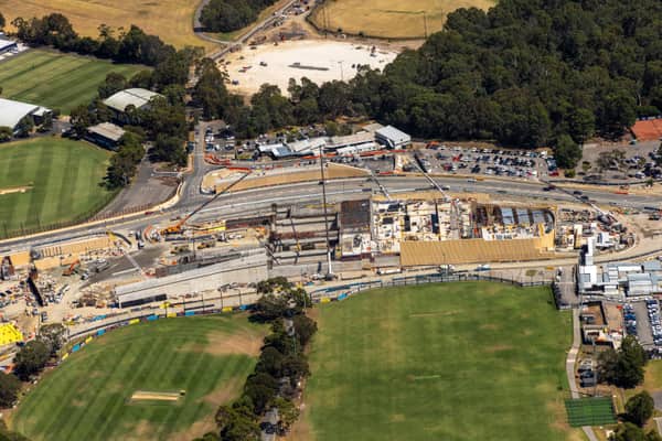 Aerial view of North East Link construction works in Bulleen VIC, with roadworks, site buildings, car parking and adjoining sports fields.