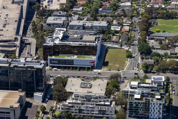 Aerial view of Westfield Doncaster beside Doncaster Road in Doncaster, showing the shopping centre edge, commercial buildings, apartments, car parks, traffic and surrounding suburban streets.