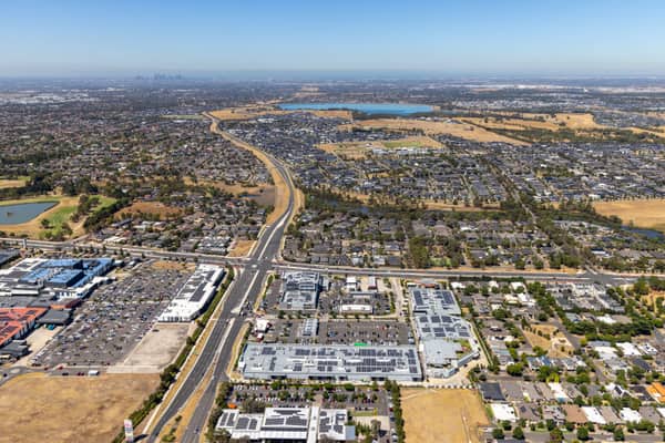 Aerial view over Craigieburn Road with retail car parks, suburban housing estates, dry paddocks and lakes in Craigieburn, Victoria.