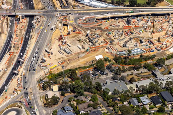 Aerial view of North East Link construction works in Bulleen, showing major road lanes, traffic, work zones, cranes and nearby residential streets.
