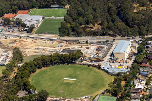 Aerial view of North East Link construction works beside Bulleen Park, showing a cricket oval, synthetic sports fields, roads, trees and nearby residential streets in Bulleen VIC.