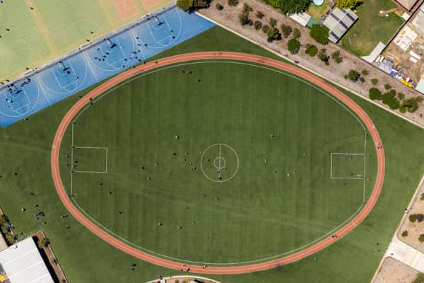 Aerial view of the sports oval, running track markings and blue hard courts beside Wedge Park Primary School on Cambrian Way in Melton West, Victoria.