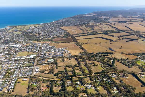 Aerial view of the Torquay coastline with residential neighbourhoods, dry farmland and the blue waters of Bass Strait in Surf Coast Victoria.