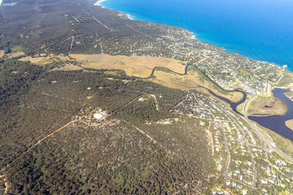 Aerial view of Painkalac Creek winding through estuary wetlands beside coastal housing, bushland and the Surf Coast shoreline at Aireys Inlet and Fairhaven in Victoria.