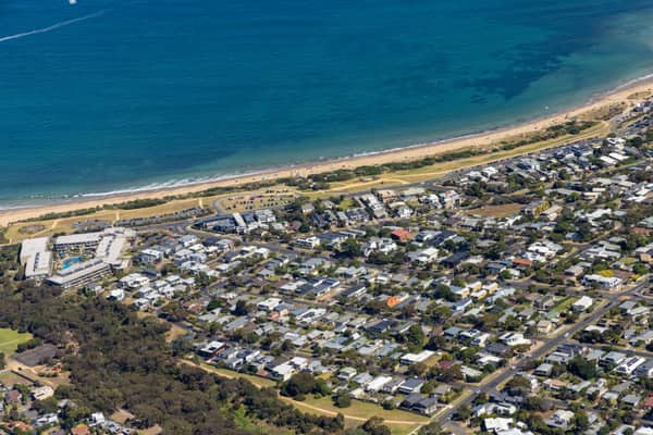 Aerial view of Fishermans Beach and The Esplanade at Torquay, with beachfront homes, resort buildings, coastal road, sandy shoreline and blue water.