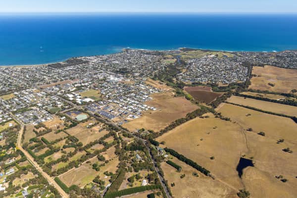 Aerial view of Torquay VIC showing the coastline, ocean, residential estates, farmland and green creek corridor.