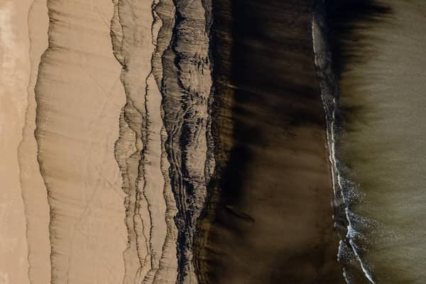 Aerial view of abstract sand, tidal debris and dark shoreline patterns on Inverloch Beach beside Bass Strait in Victoria.